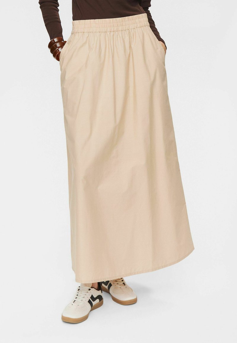 Beige maxi sukně vyrobená z lehké tkaniny, s elastickým pasem a kapsami, doplněná béžovými a černými teniskami.