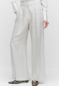 Witte, wijde broek met een gladde satijnen afwerking, voorzien van voorplooien en een getailleerde pasvorm. Gecombineerd met schoenen met een slangenhuidpatroon.