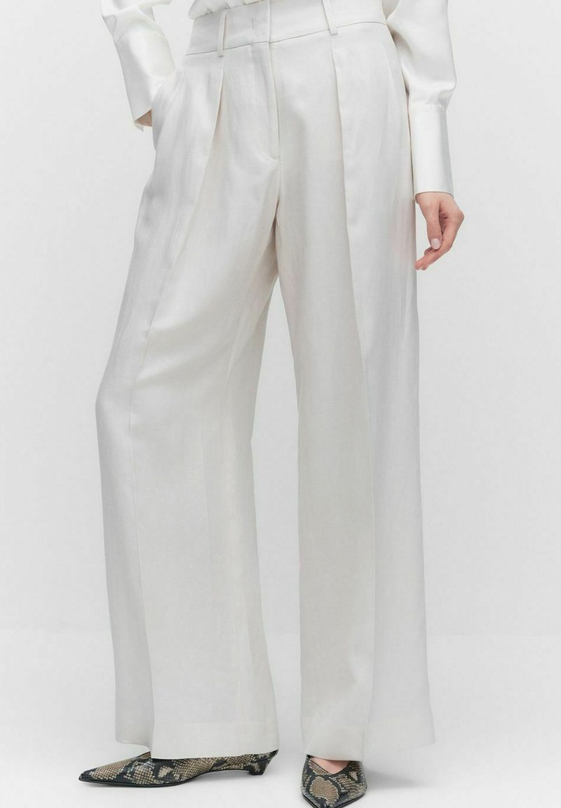 Witte, wijde broek met een gladde satijnen afwerking, voorzien van voorplooien en een getailleerde pasvorm. Gecombineerd met schoenen met een slangenhuidpatroon.