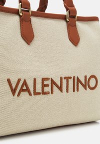 Borsa a tracolla in tessuto beige con manici in pelle marrone e "VALENTINO" ricamato in grandi lettere marroni sul davanti.
