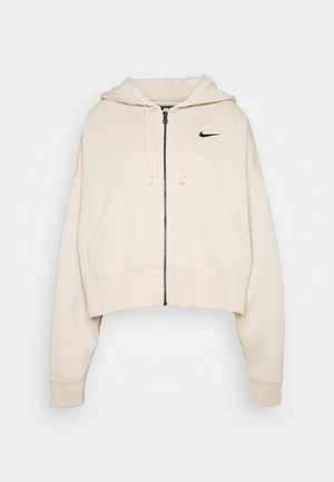 Sweat à capuche beige court zippé avec poches avant, capuche réglable avec cordon, manches longues et petit logo Nike noir sur la poitrine.