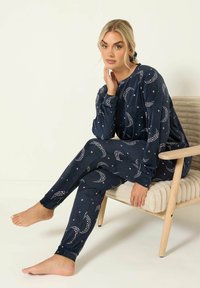 Pigiama blu navy realizzato in morbido tessuto, con stampe di lune crescenti e stelle bianche; maniche lunghe e pantaloni aderenti.