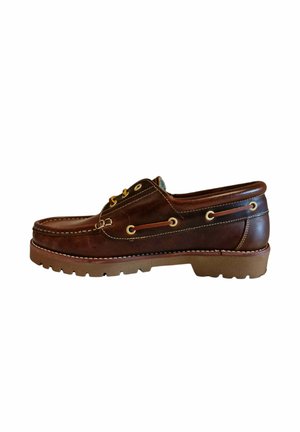 Zapato de barco de piel marrón con costuras blancas, ojales de metal y suela de goma. Presenta un diseño bajo y redondeado, con una superficie texturizada.