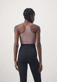 Smeđi sportski crop top s dizajnom racerback, uparen s crnim tajicama visokog struka. Glatka tkanina s prilagođenim siluetom.