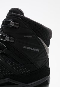 Botas de senderismo de caña alta negras, hechas de malla y materiales sintéticos, con la marca Gore-Tex, patrones texturizados y acentos en gris contrastante.