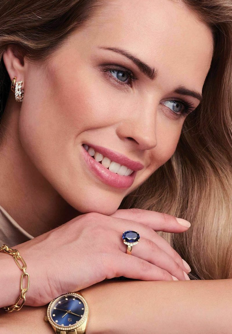 Gul bracelet, klocka med blå urtavla och juvelaccenter, samt en blå stensring. Släta ytor; elegant design och distinkt färgkontrast.