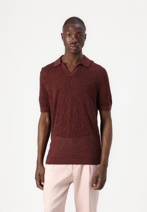 Polo shirt bordeaux à manches courtes avec un motif en dentelle texturée, col en V, et col et poignets contrastés. Porté avec un pantalon rose pâle.