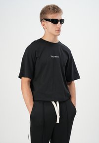 Black short-sleeve t-shirt with a small white logo, paired with black pants featuring a white drawstring. Accessories include black sunglasses.
