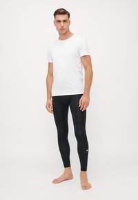 White short-sleeve t-shirt paired with fitted black leggings, featuring a small white Nike logo on the lower leg. Smooth fabric, athletic fit.