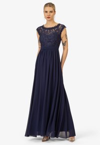 Navyblauwe jurk met een kanten lijfje en korte mouwen, vloeiende rok, cincte taille en doorschijnende overlay. Glanzende schoenaccenten.