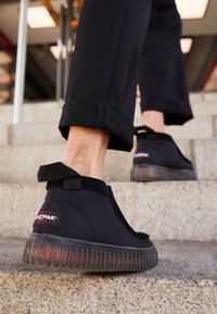 Personne portant des baskets Fastpak noires et un pantalon noir montant des escaliers en béton dans un environnement urbain.