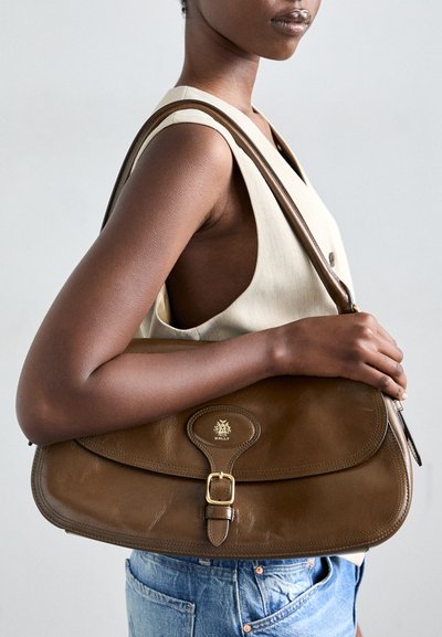 Brown leather shoulder bag with a rounded shape, featuring a gold-tone logo, buckle accent, and textured surface.
