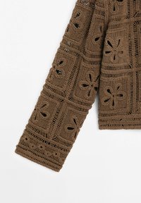 Manche de pull marron en crochet avec des motifs floraux et géométriques ajourés sur fond blanc.