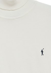 Pull à col roulé couleur crème avec un petit logo brodé représentant une personne portant une clé de golf sur le bas à droite.