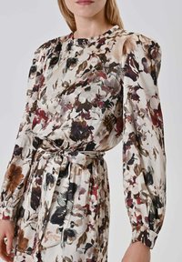 Vestito floreale in tessuto leggero con maniche lunghe a sbuffo, scollo tondo e vita con cintura. Presenta un motivo floreale multicolore su sfondo chiaro.