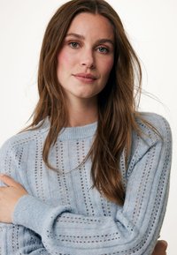Světle modrý pletený svetr s měkkou texturou, který má vertikální pruhy s vyšívaným vzorem a žebrované manžety. S jednoduchým designem kulatého výstřihu.
