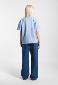 Camiseta de algodón azul claro con mangas cortas, combinada con pantalones vaqueros oscuros de pierna ancha, que presentan un ajuste relajado y un diseño casual.