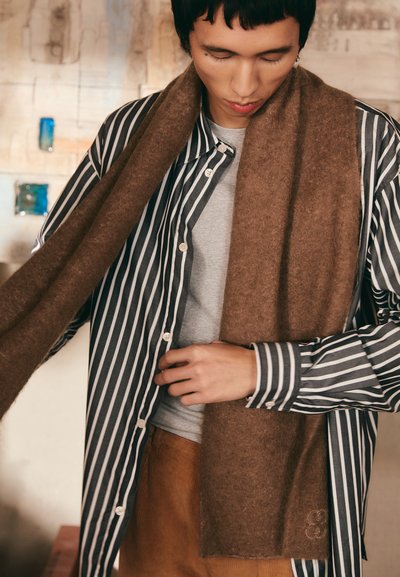 Brown scarf made of soft fabric, draped around the neck, paired with a black and white striped button-up shirt over a gray t-shirt.