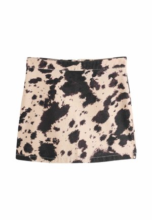 Mini-jupe beige avec motif irrégulier imprimé vache noire, ourlet droit et coutures visibles le long de la ceinture et du bas.