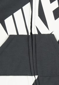 Mikina Nike z tmavo šedej látky s veľkými bielymi geometrickými vzormi, prednými vreckami a dizajnom na zips.