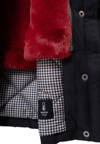 Forro de piel sintética roja, tejido acolchado de cuadros en blanco y negro, y exterior negro con cremallera y botones a presión etiquetados como "Warm Chaud."