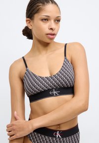 Μαύρο και λευκό σουτιέν με επαναλαμβανόμενο μοτίβο «CK», που διαθέτει λεπτές τιράντες και φαρδύ ελαστικό λάστιχο με το λογότυπο «Calvin Klein» στο κέντρο.
