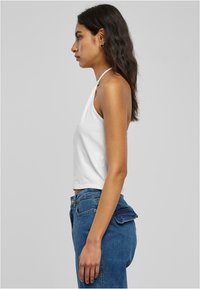 Haut court blanc à bretelles fabriqué en coton, avec un design simple. Associé à un jean en denim bleu taille haute avec un détail de poche.