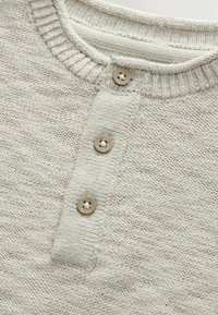 Pull en tricot gris clair avec un col rond, trois boutons marron et une texture côtelée sur le col et la patte de boutonnage.