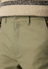 Olive green pants made of textured fabric, featuring a button closure with "HUGO JEANS" engraved. Pockets are on the front seams.