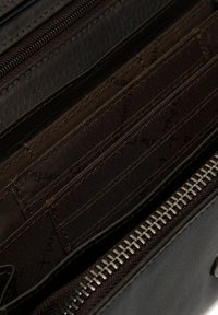 Interno di un portafoglio in pelle nera che mostra più scomparti per carte con una texture liscia; presenta una cerniera argentata e foderatura in tessuto marrone.