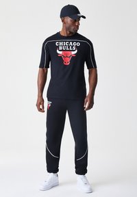 Crna majica kratkih rukava i trenirke s crvenim logotipom Chicago Bullsa. Bijeli naglasci šivanja i bijele tenisice upotpunjuju odijelo.