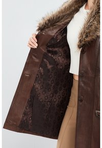 Brown leather coat with faux fur collar, featuring a circular patterned interior lining and visible buttons along the front.