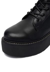 Czarna skórzana shoe z okrągłym noskiem, sznurowanym designem oraz grubą czarną podeszwą platformową z kontrastującą przeszywaną krawędzią.