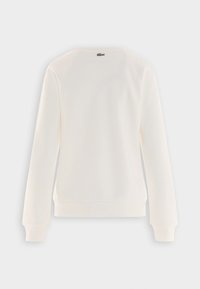 Sudadera color crema con cuello redondo, mangas raglán y pu�ños acanalados. Presenta una pequeña etiqueta con el logo en la parte posterior, cerca del cuello.