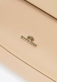 Beige leather surface with gold Wittchen brand logo and emblem centered, showcasing fine stitching detail along edges.