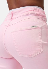 I jeans di denim rosa presentano una cintura elasticizzata con una texture arricciata e una tasca posteriore con un piccolo cartellino logo.