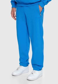 Blaue Sweatpants aus weichem Stoff mit lässigem Schnitt, ausgestattet mit Reißverschlusstaschen und gerippten Bündchen, kombiniert mit weißen Sneakern.