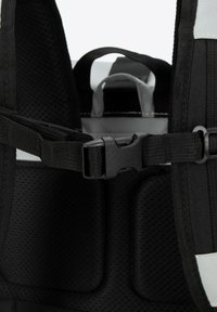 Intérieur d'un sac à dos noir comportant un tissu rembourré et texturé, des bretelles réglables et une fermeture à boucle en plastique au niveau de la poitrine.
