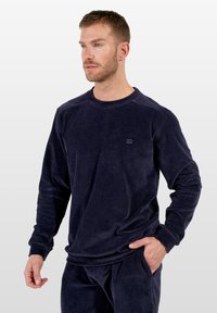 Camisa de manga larga de pana en color marino con textura acanalada y cuello redondo, que presenta un sutil logo en el pecho y puños ajustados.