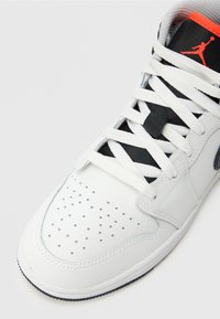 Λευκό παπούτσι μπάσκετ με διάτρητο μπροστινό μέρος, μαύρο σύστημα κορδονιών και πορτοκαλί λεπτομέρεια στη γλώσσα. Διαθέτει λείο δερμάτινο φινίρισμα.