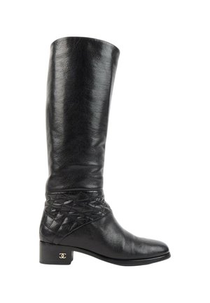 Botte noire en cuir montante jusqu'au genou avec un petit talon, détail matelassé autour de la cheville et un petit logo doré sur le talon.