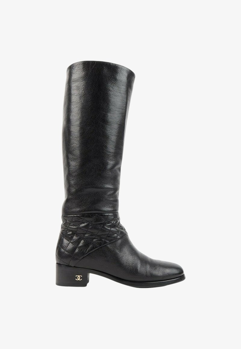Botte noire en cuir montante jusqu'au genou avec un petit talon, détail matelassé autour de la cheville et un petit logo doré sur le talon.