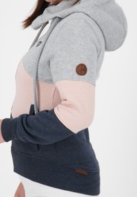 Felpa con cappuccio in grigio, rosa e blu navy; presenta un cordino, polsini a coste e una toppa in pelle con logo sulla manica. Design casual e tessuto texturizzato.