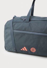 Mørkeblå sports duffelbag lavet af slidstærkt stof. Har orange Adidas-logo og Bayern München-emblemet, samt lynlåskompartementer og håndtag.