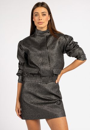 Zwarte cropped jas van textuurstof, met hoge kraag en gepuffte mouwen, gecombineerd met een bijpassende mini-jurk van textuurstof.