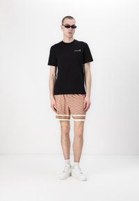 Czarna bawełniana koszulka z krótkim rękawem, w połączeniu z pomarańczowymi spodniami w wzory, z geometrycznym wzorem i białymi paskami na brzegach. Białe trampki.