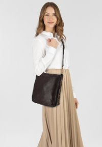 Borsa a spalla in pelle marrone con una texture liscia e ricami decorativi lungo un bordo. La borsa presenta una lunga tracolla regolabile.