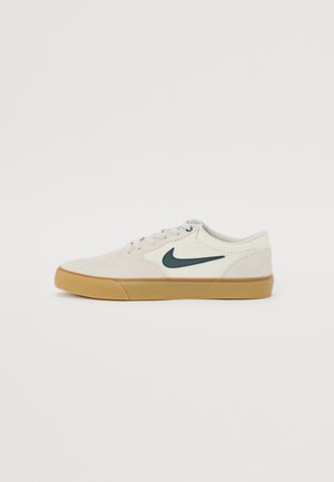 Sneaker Nike bianco basso con logo swoosh nero e suola in gomma color marrone, mostrato di lato su sfondo semplice.
