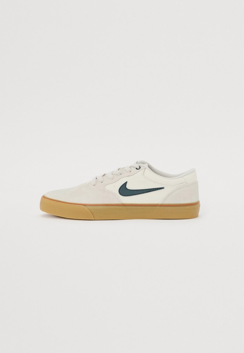 Baskets basses blanches Nike avec logo swoosh noir et semelle en caoutchouc couleur gomme, vues de profil sur un fond uni.