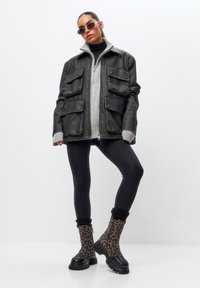Giacca oversize in pelle nera con fodera grigia, quattro tasche anteriori, abbinata a leggings neri e stivaletti con stampa leopardata.